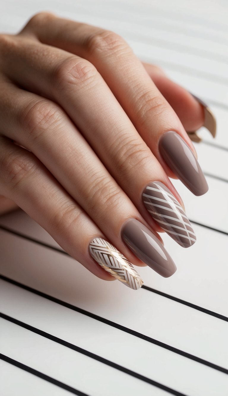 Hand with soft taupe nails featuring layered white diagonal lines, paired with a beige nail detailed in shiny gold leaf-inspired striping.