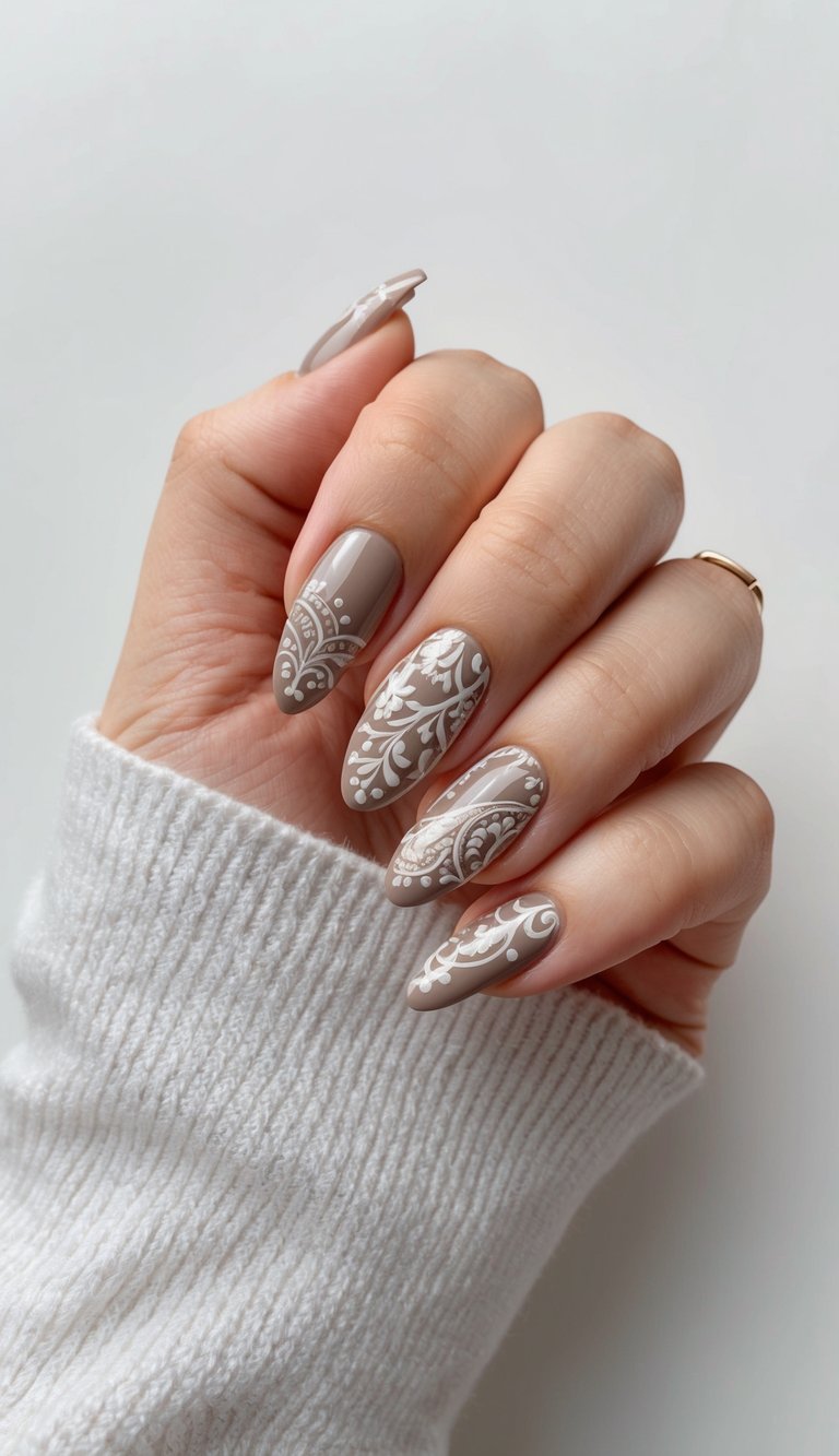 Hand with glossy taupe nails decorated in detailed white lace-style designs, adding a soft, elegant finish to a neutral palette.