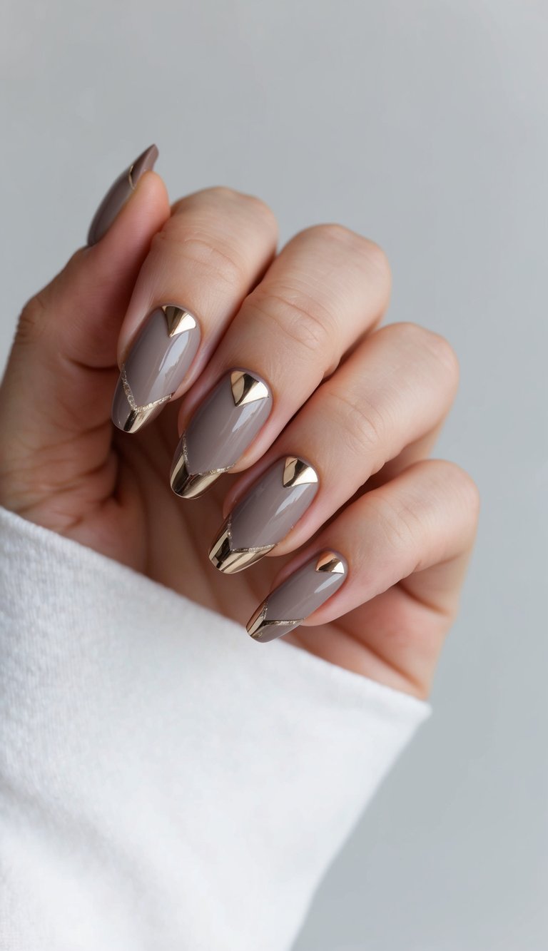 Glossy taupe nails with sharp gold chrome chevron tips and cuticle accents for a modern, luxe manicure look.