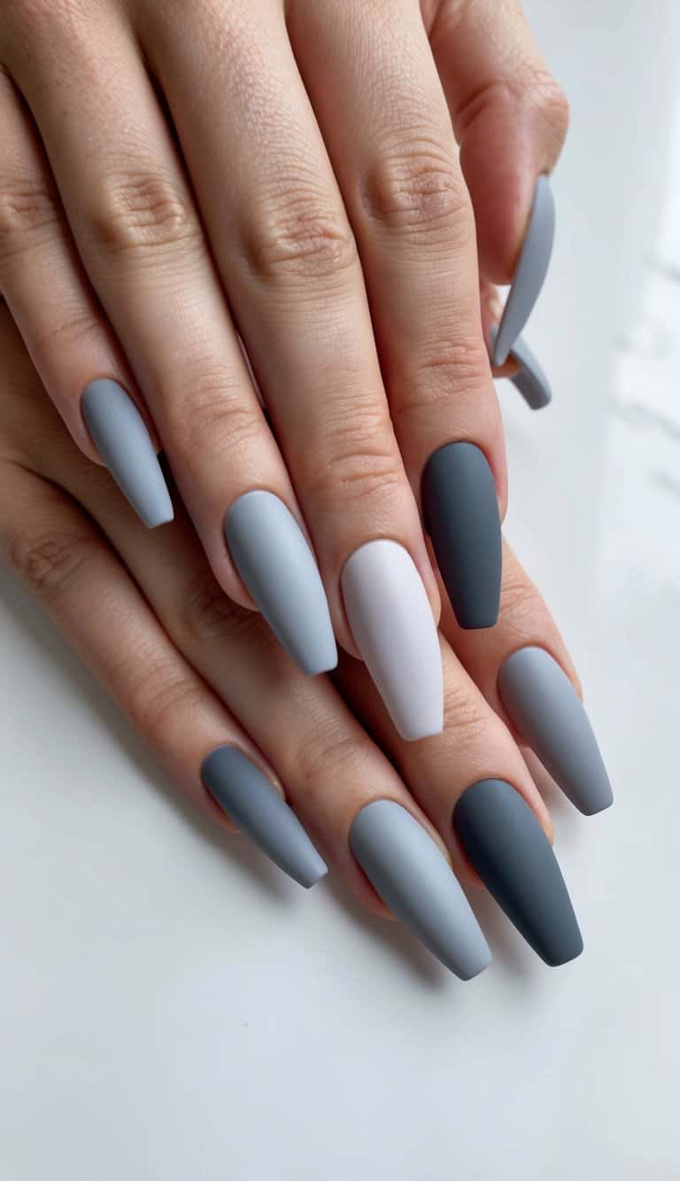 A set of matte gray nails arranged in a gradient fade pattern on a clean, minimalist background
