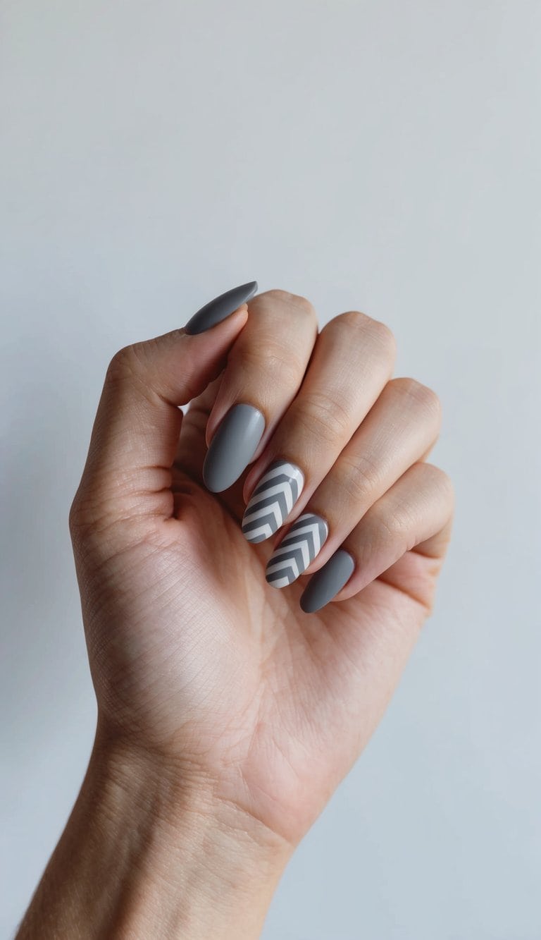 A hand holding a matte gray nail with chevron zigzag design against a clean, minimalist background