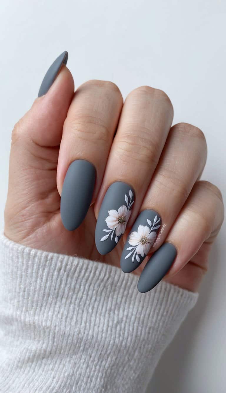 A close-up of matte gray nails adorned with delicate floral designs on the ring finger