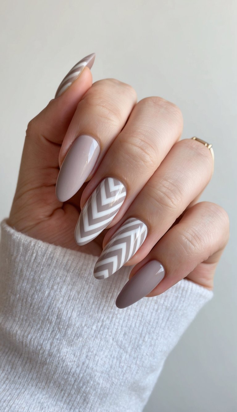 A close-up of a hand with sleek, chevron-patterned minimalist nail art in a modern color palette