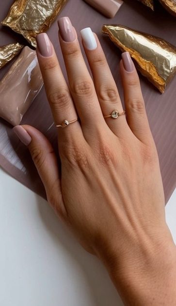 A table covered in mauve and gold foil nail art supplies, with various shades of soft dusty pink and neutral colors