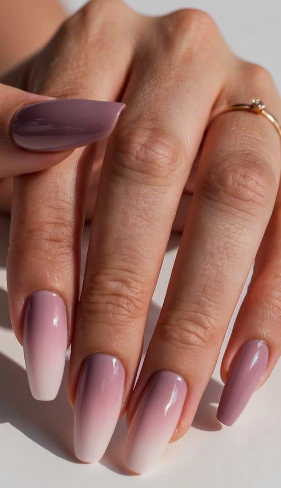 A close-up of mauve nails with soft pink hues and a gradient shine, set against a neutral background