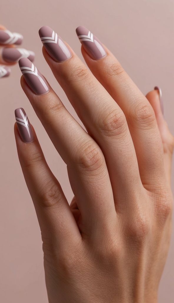 A trail of chevron-shaped mauve nail art designs on a soft dusty pink background