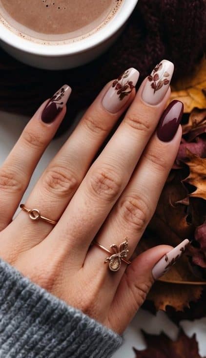 A maroon nail art design with deep burgundy polish and nude accent nails, featuring brown leaf patterns for a stylish autumn-inspired look.