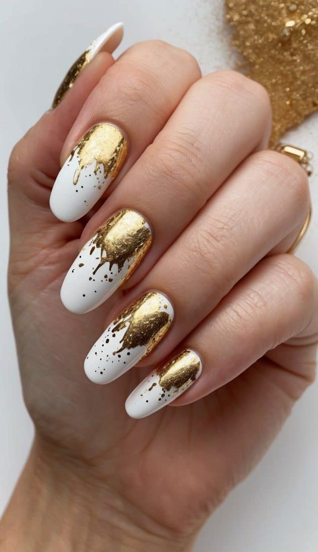 Gold splatter over white nails, creating a luxurious and elegant nail art design