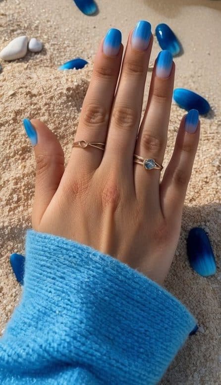 A sandy beach with waves crashing on the shore, surrounded by ocean blue ombre nails scattered across the sand