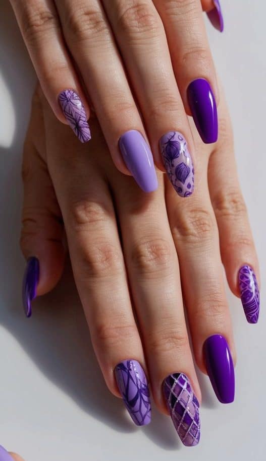 A close-up view of various purple nail art designs on a clean, manicured surface, showcasing intricate patterns and details