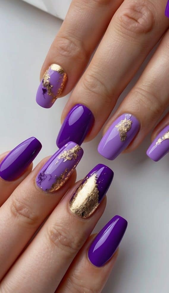 A close-up view of various purple nail art designs, with gold foil accents and hints of lilac, arranged on a clean, minimalist background
