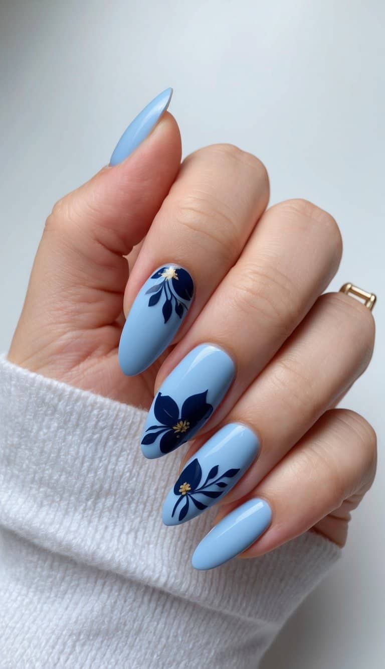 Stylish sky-blue nails with navy floral designs and gold accents, adding a sophisticated yet fun touch to this cute blue nail art look.