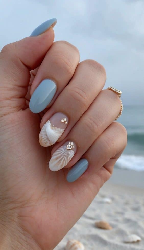 A soft blue manicure with 3D seashell details and delicate gold accents, creating an elegant and beach-inspired nail art look.