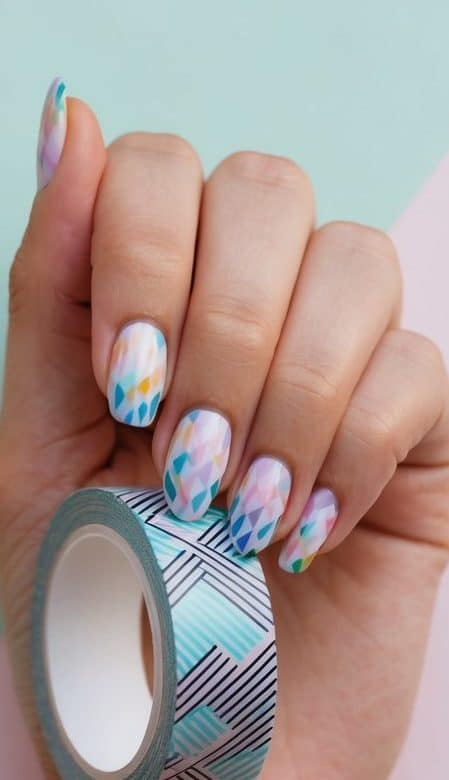 A hand holding a roll of geometric patterned tape against a pastel colored background