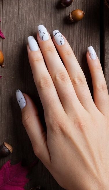 A close-up of autumn nail art featuring a white base with intricate black branch designs, offering a modern and nature-inspired seasonal look.