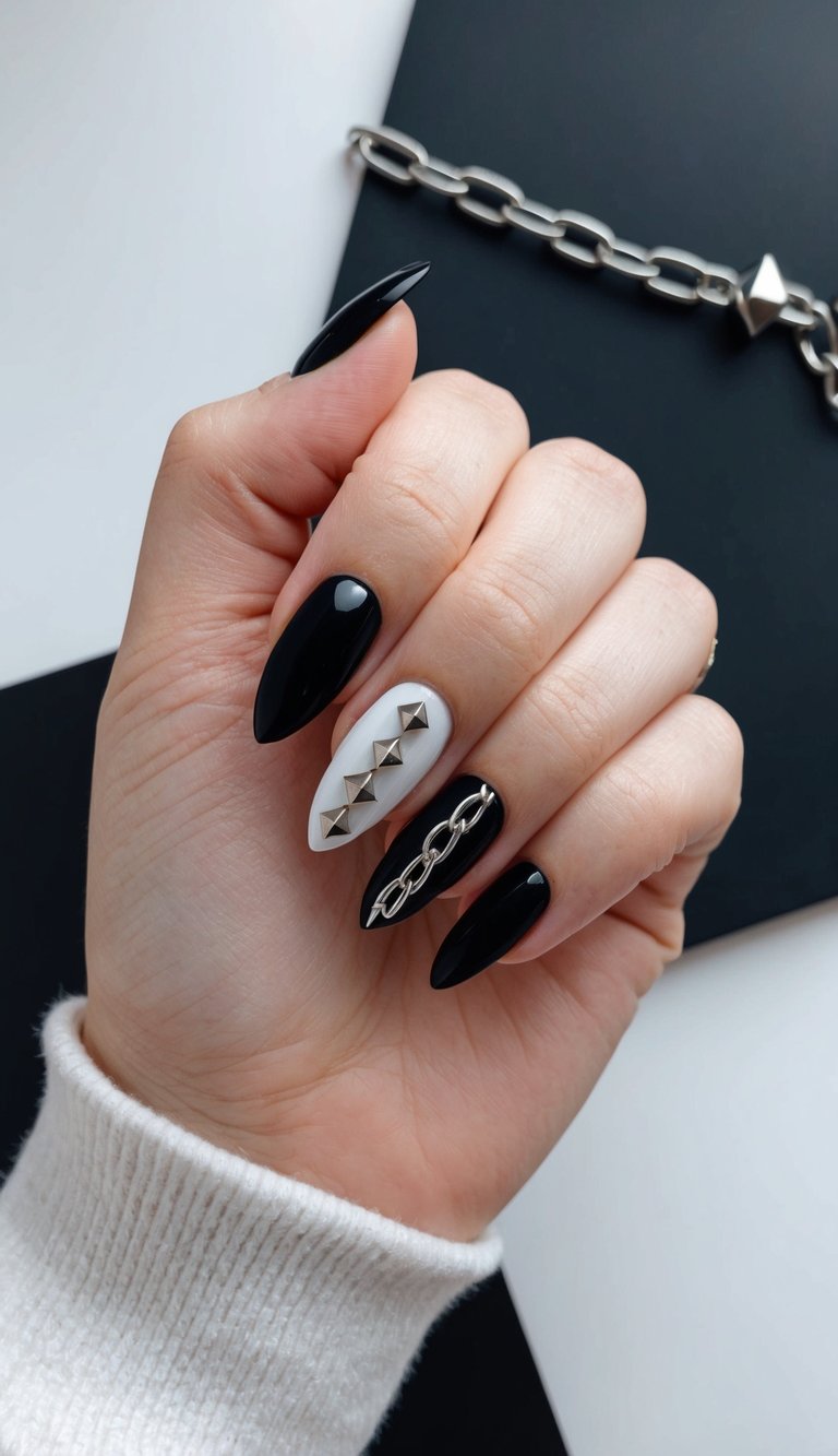 High-gloss black nails with silver studs and a chain detail over white for a bold emo-glam nail look.