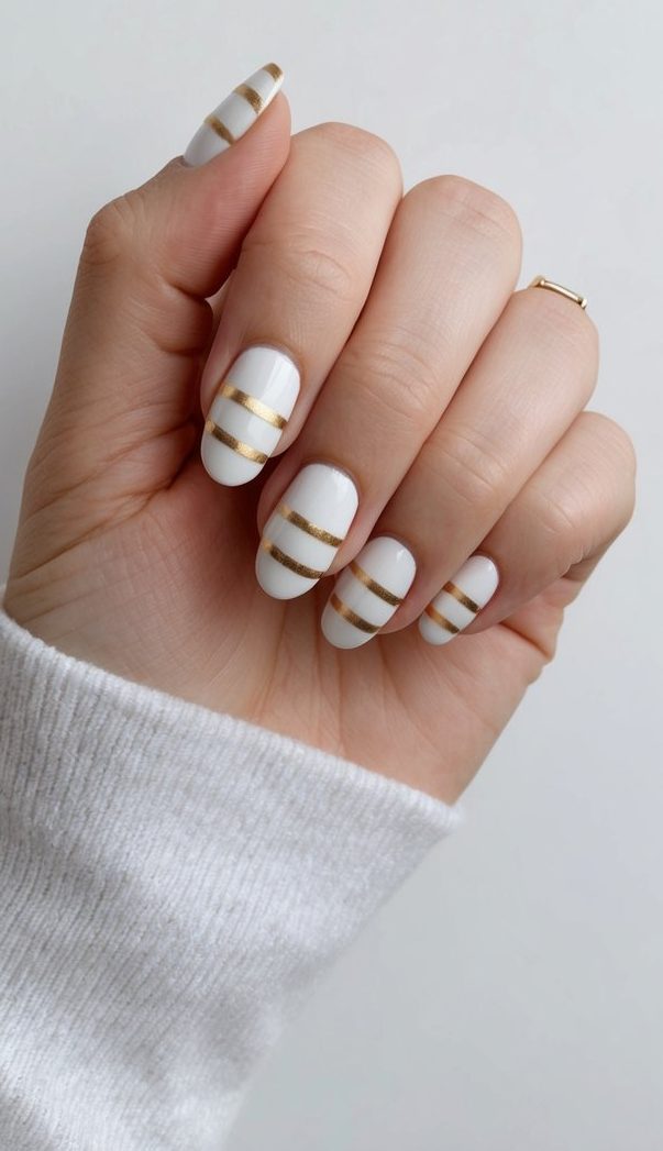 A hand with minimalist gold stripes on nails against a white background