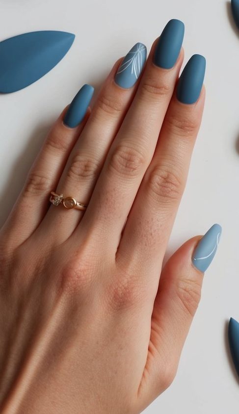 A collection of matte dusky blue nail art designs displayed on a clean, white surface with various shapes and patterns