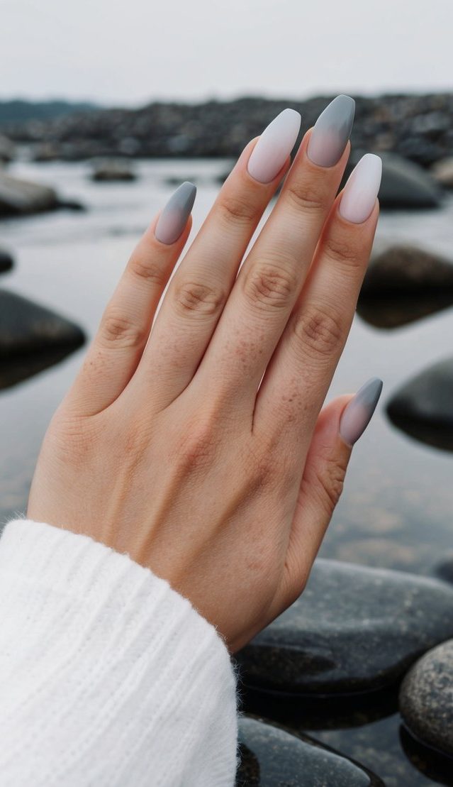 Smooth gray ombre nails resting on reflective river rocks