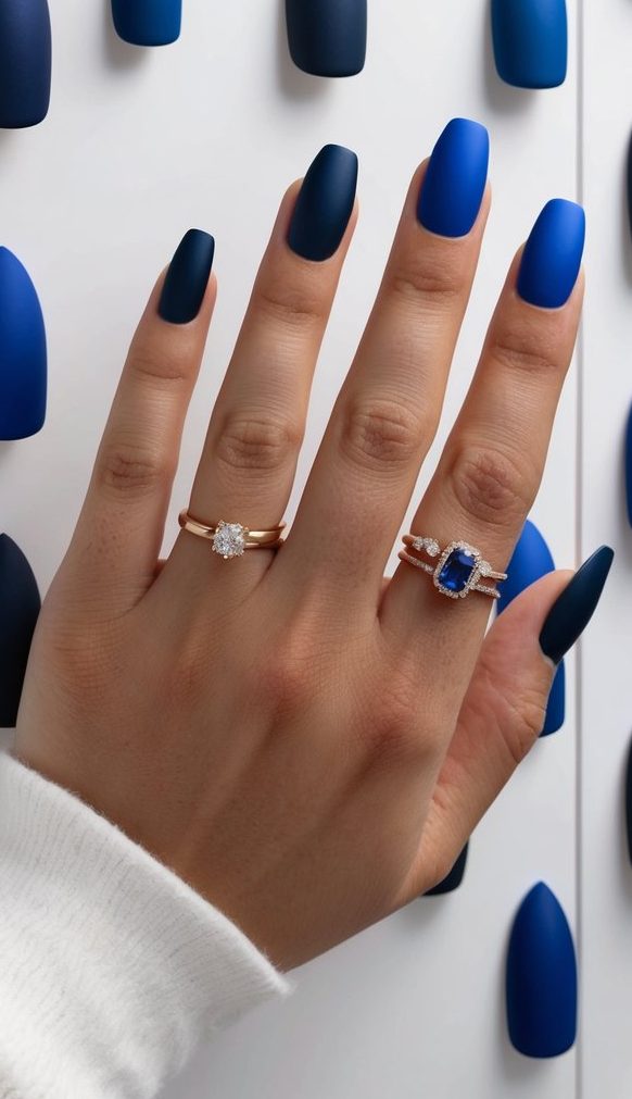 A collection of 50 jewel-toned blue matte nail art designs displayed on a sleek, minimalist backdrop