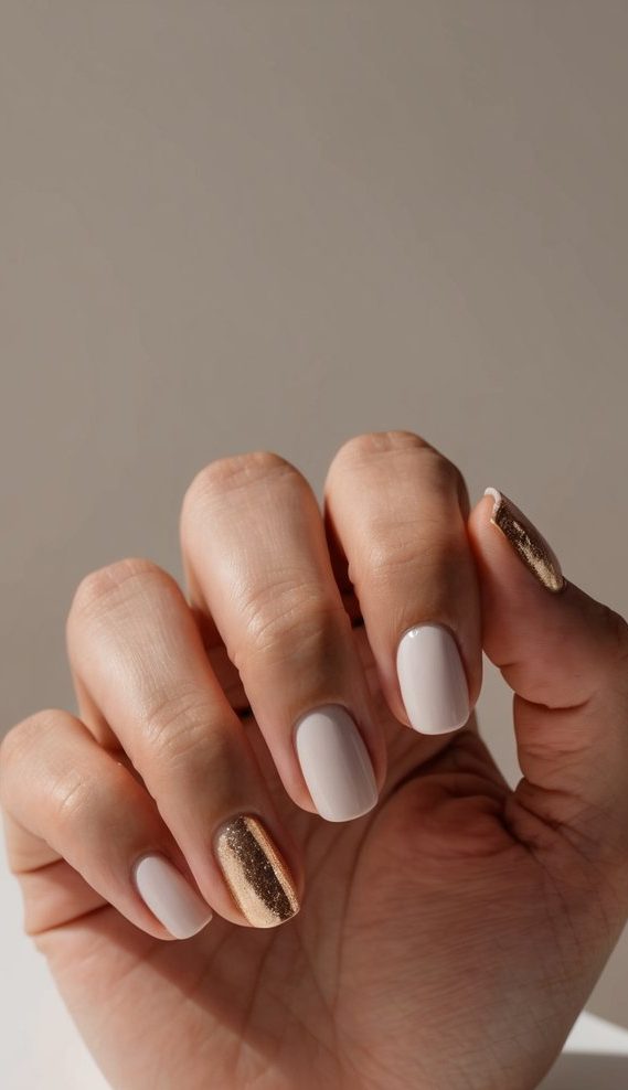 A hand with minimalist nail art featuring gold cuticle accents against a neutral background