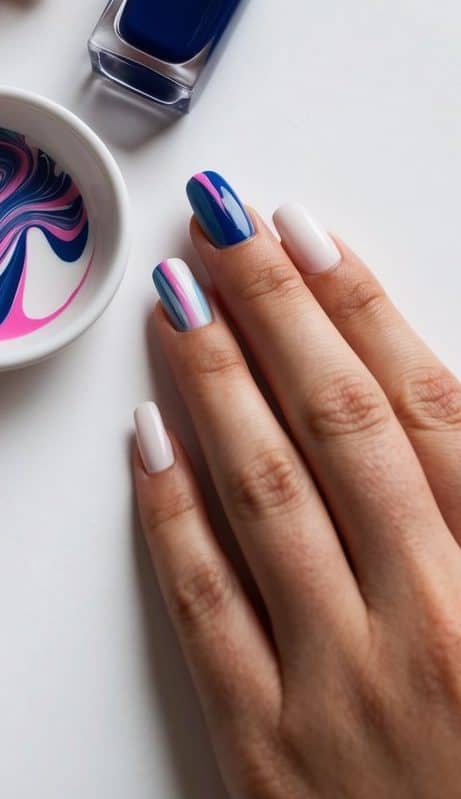 A small dish of marbling paint, a nail polish bottle, and a clean nail surface