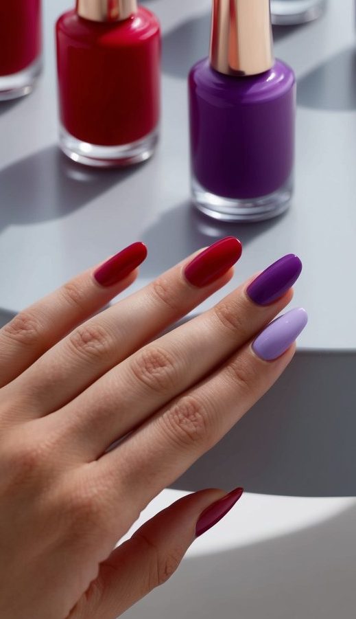 A close-up of red and violet nail polish bottles arranged on a sleek, modern surface