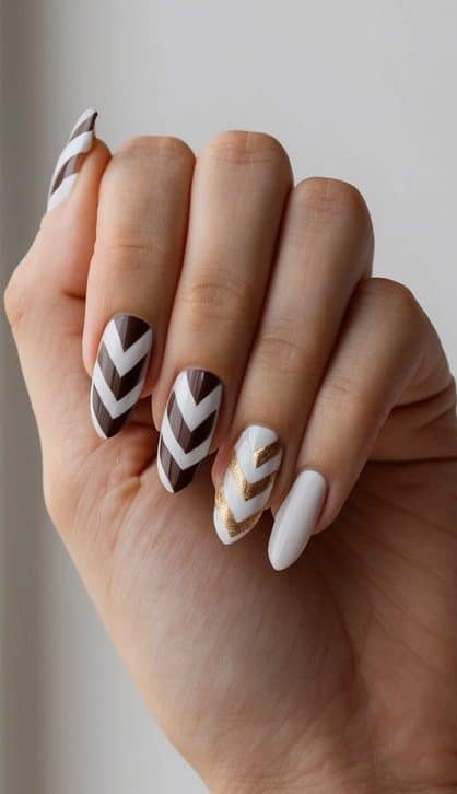 A hand with a dual-tone chevron manicure against a simple, elegant background