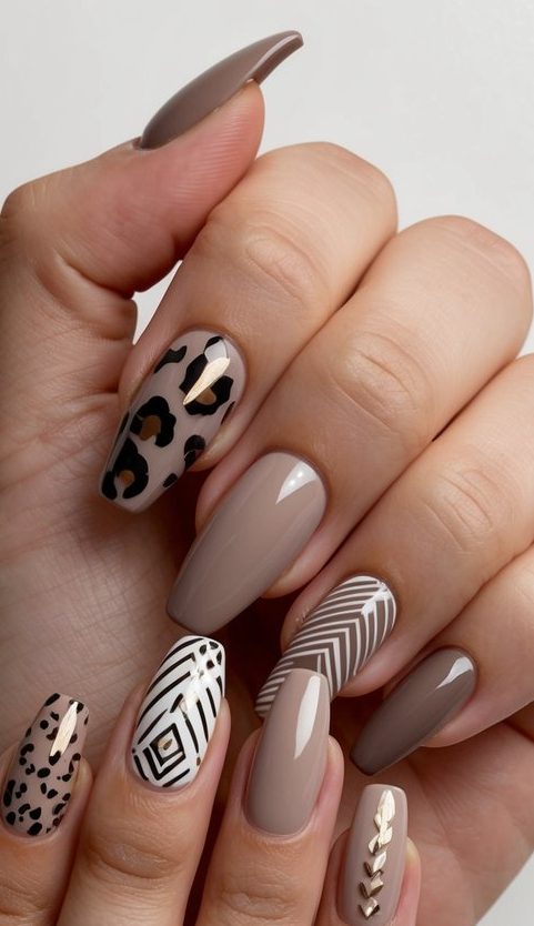 Taupe nails featuring a mix of leopard spots, bold white geometric lines, and gold foil accents for a stylish and eclectic nail art look.