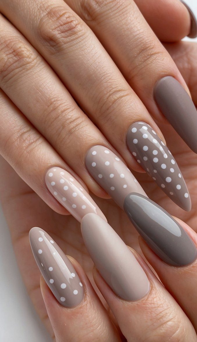 Close-up of almond taupe nails featuring white dots across soft nude and grey bases for a subtle retro vibe.