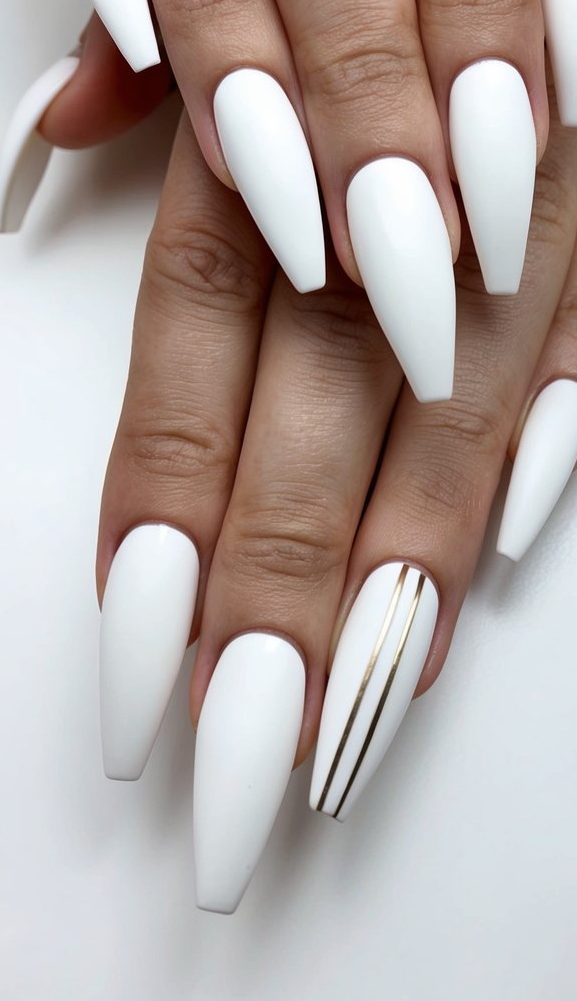 Matte white coffin nails with minimal gold striping detail on the ring finger for a sleek look.