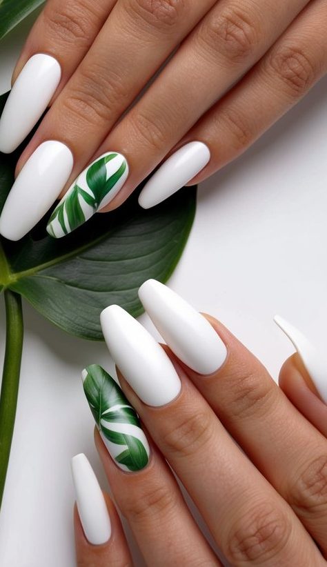 Matte white nails with leafy green botanical accents on two fingers, styled above a real tropical leaf.