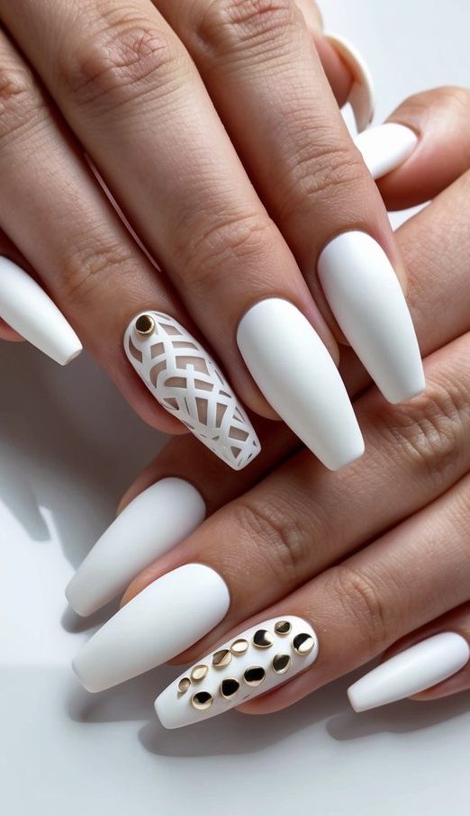 Close-up of matte white nails featuring a cutout lattice design and bold gold metal studs for a modern luxury look.
