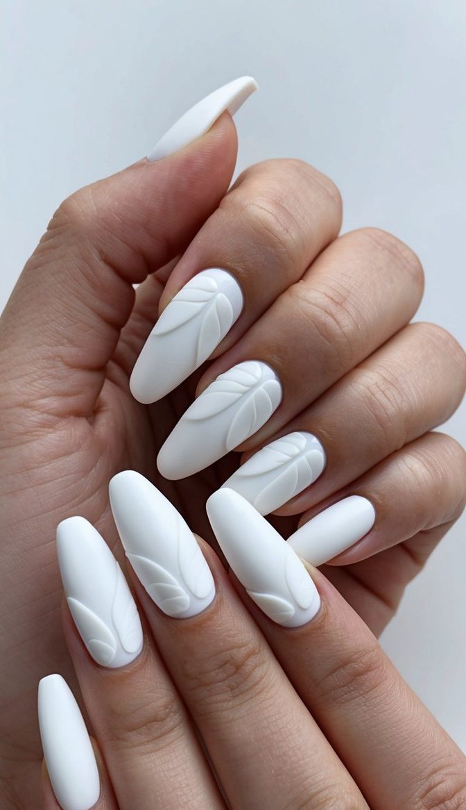 Close-up of matte white nails with embossed botanical details, blending minimalist style with elegant 3D nail artistry.