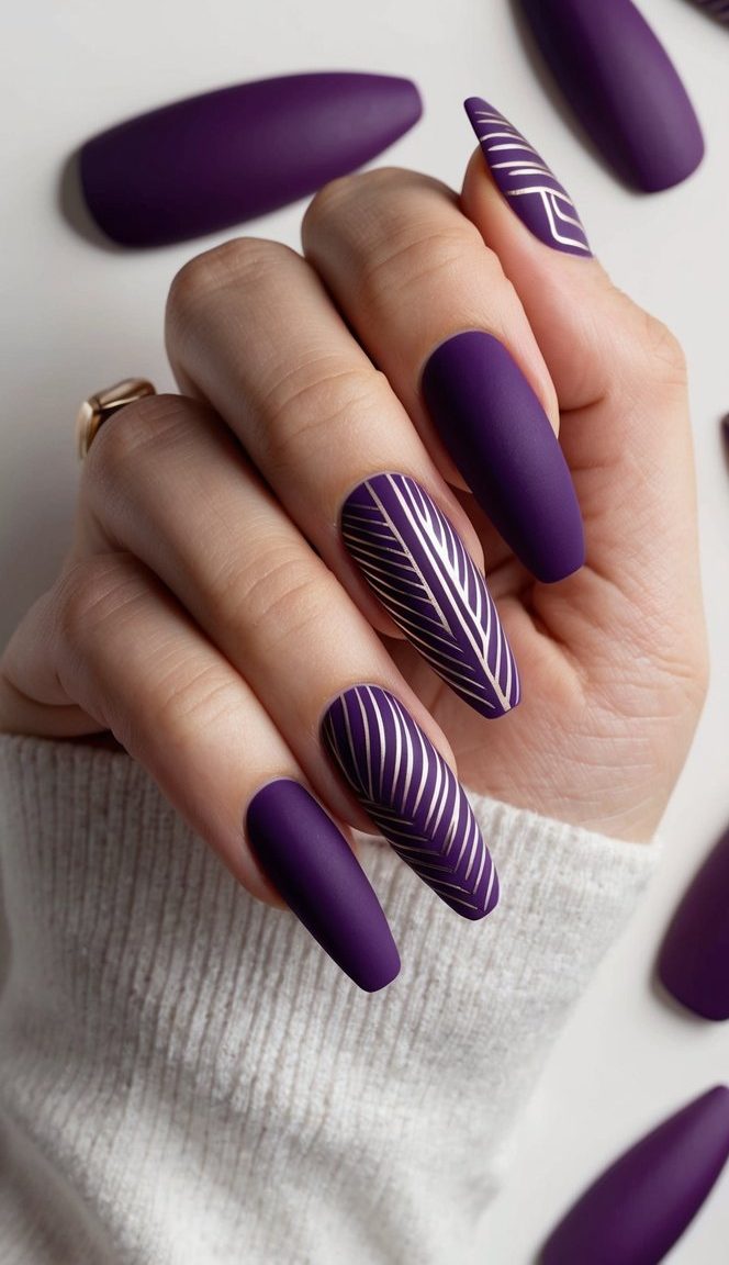 Close-up of almond-shaped matte purple nails, accented with sleek white diagonal and leaf-pattern lines for a bold design twist.