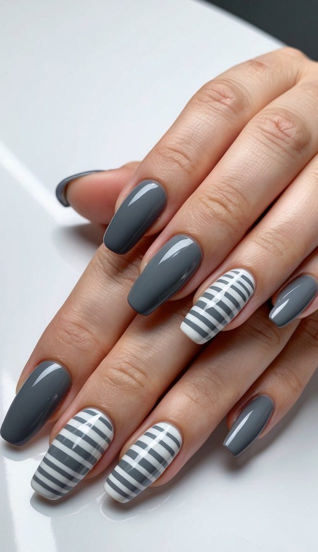 Hand with glossy charcoal gray nails paired with striped white accent nails featuring clean black-gray lines for contrast.