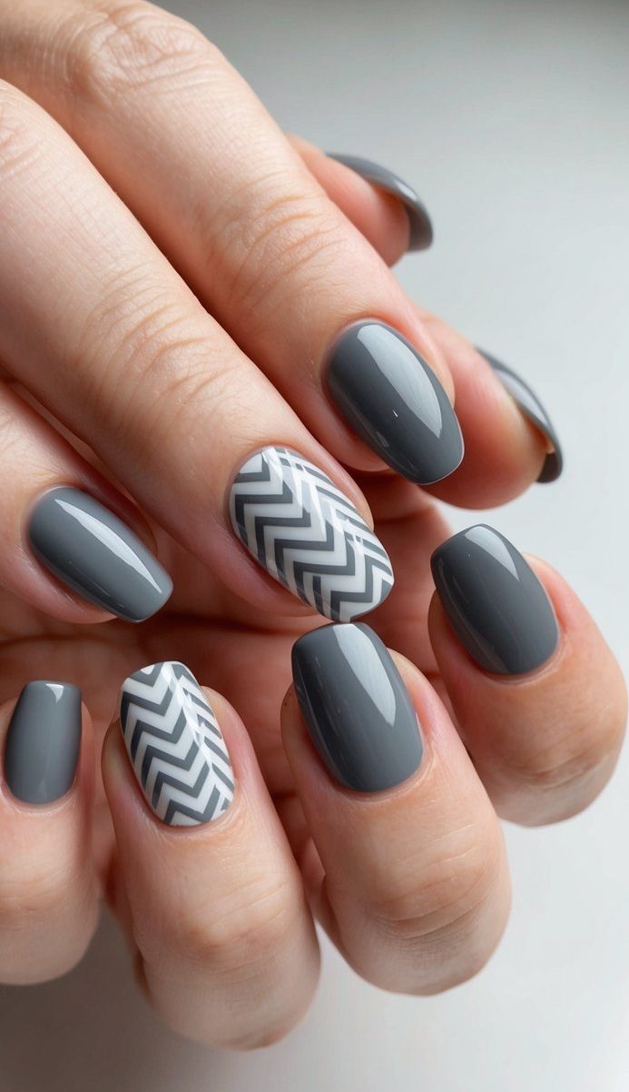 Glossy dark gray nails with sharp white chevron accent patterns that add a modern, geometric edge to the manicure.