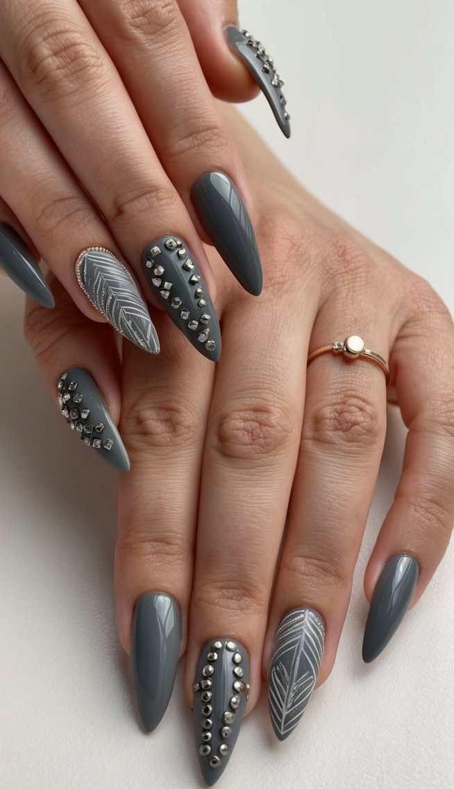 Sharp gray nails featuring silver metal accents and fine leaf-inspired designs for a creative, edgy manicure.