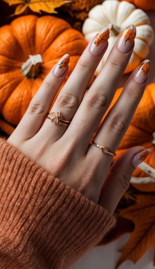 Nude nails with delicate orange leaf art, surrounded by pumpkins and fall decor, capturing a warm and cozy autumn aesthetic.