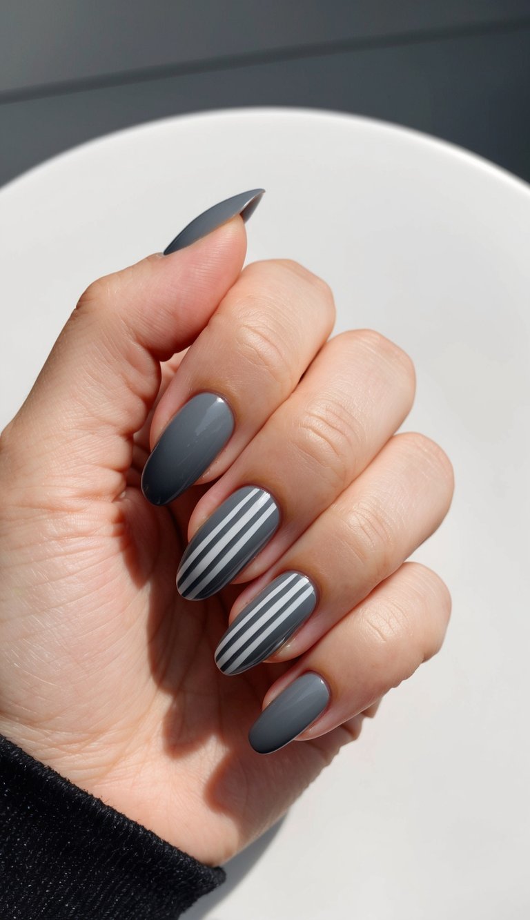 Matte charcoal nails with vertical white stripes on two fingers, showcasing a clean and minimalist striped nail art design.