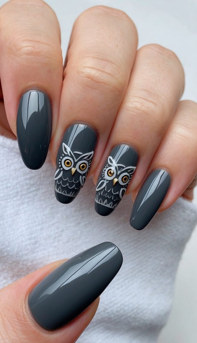 Dark gray nails with shiny finish and cute owl artwork with gold eyes, creating a whimsical and stylish design.