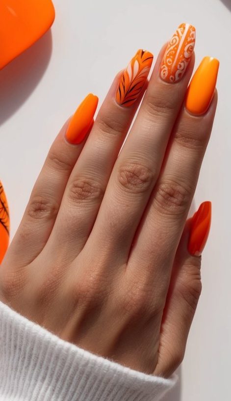 Vivid orange nail design featuring dramatic feather accents and detailed swirl art for a bold, stylish effect.
