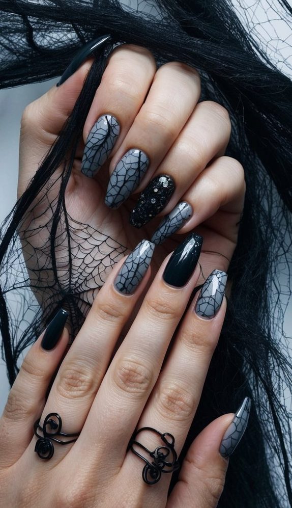 Matte grey nails with spiderweb detailing, paired with glossy black polish and a sequin-covered accent for a glam-goth Halloween design.