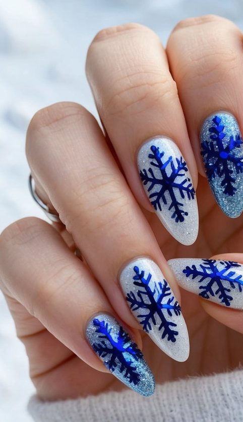 Glittery silver and icy white nails decorated with metallic blue snowflakes for a Frozen-inspired holiday nail look.