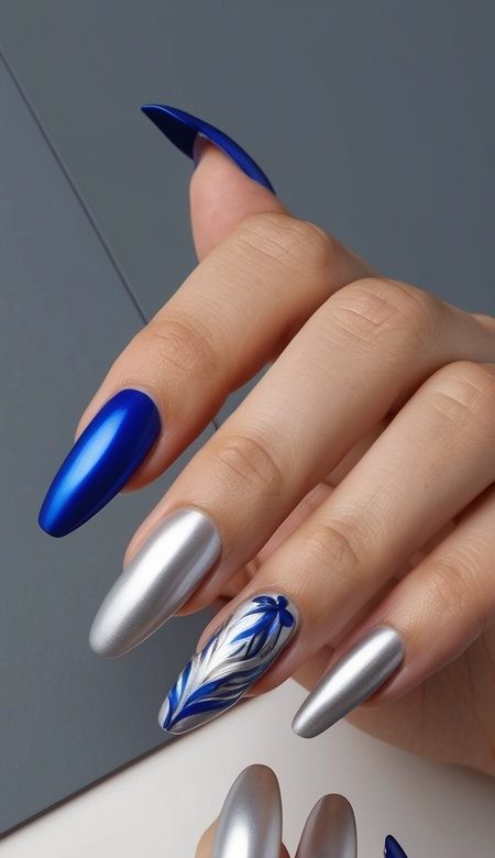 Matte cobalt blue and chrome silver nails with a delicate blue feather design, creating a sleek and modern nail art look.