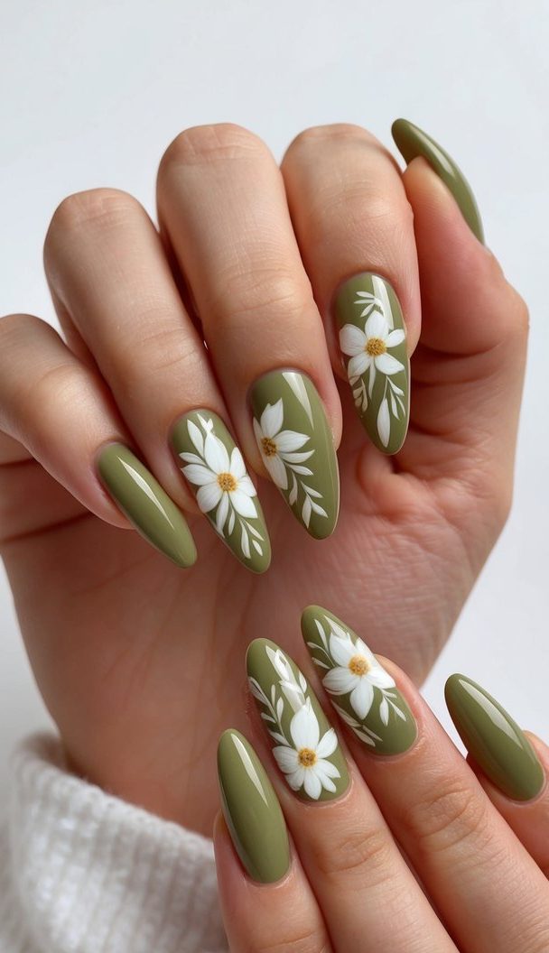 Close-up of soft olive green nails decorated with dainty white daisies and tiny golden centers, exuding a gentle floral charm.