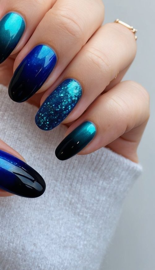 Almond-shaped nails with glossy black-to-teal ombré, accented by one teal glitter nail and one bright blue polish with a mirror shine.