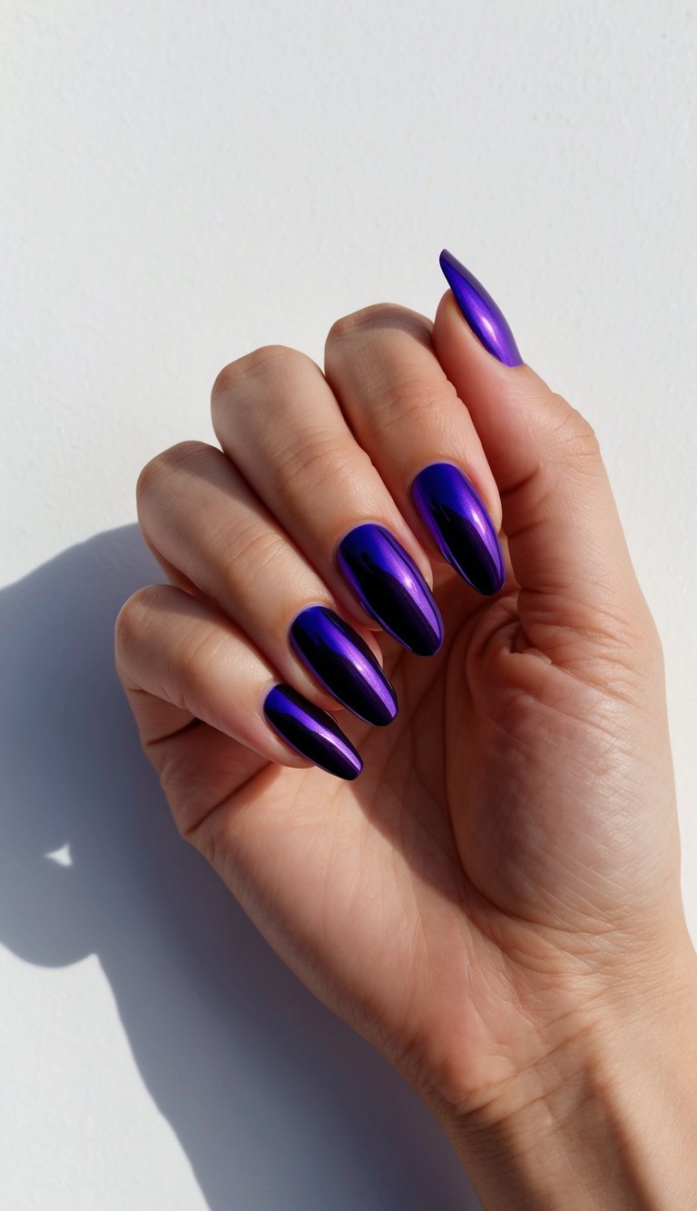 Hand with sharp almond nails in dark violet chrome, reflecting light for a modern, high-gloss style.