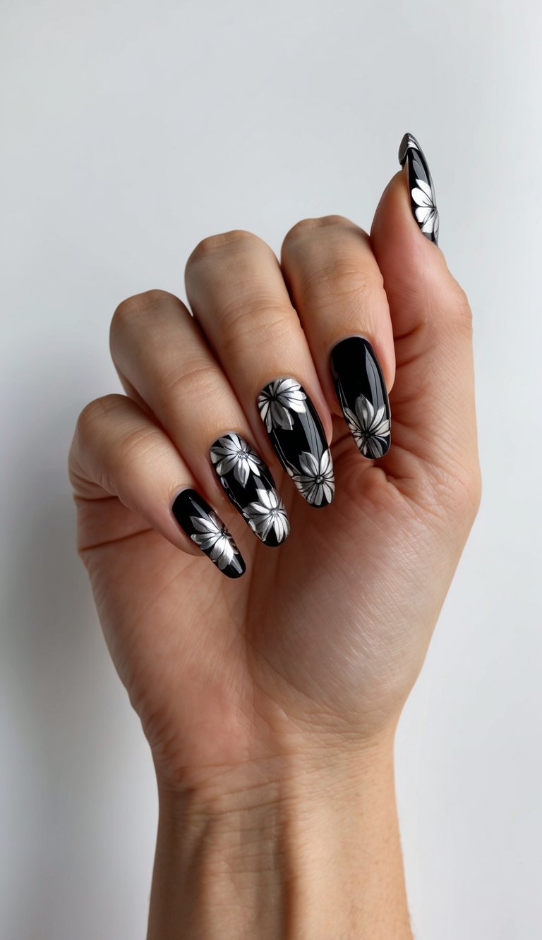 Hand showing sleek black nails topped with silver daisy floral accents, creating a bold yet delicate contrast.