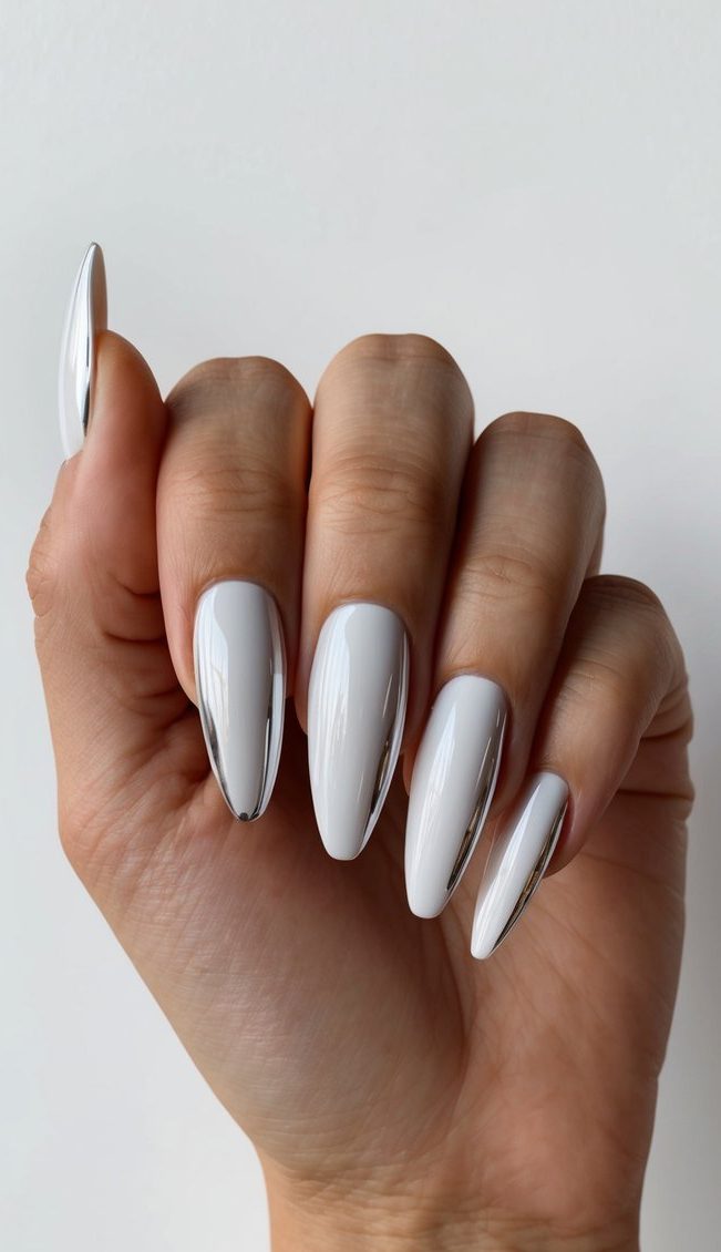 A hand holding a mirror-like white chrome nail with sleek and sophisticated designs